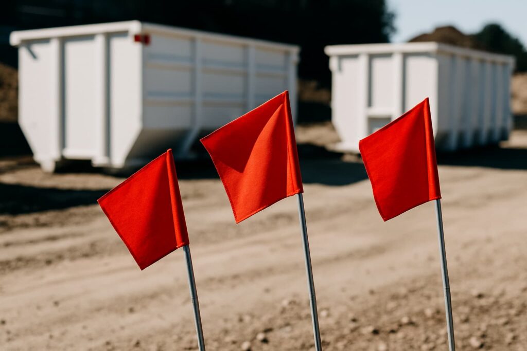 warning flags on construction site with dumpsters in background to depict dumpster rental red flags as a caution to do research before paying